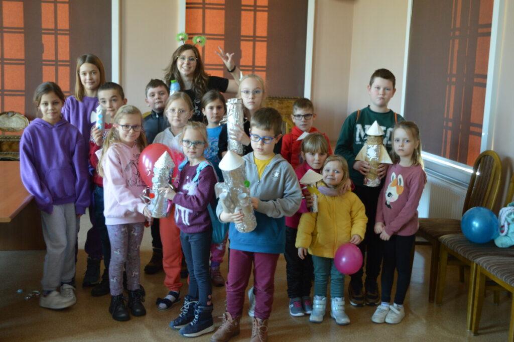 Ferie zimowe 2023 - grupa dzieci i ich opiekunowie, dzieci trzymają papierowe rakiety - zdjęcie grupowe 