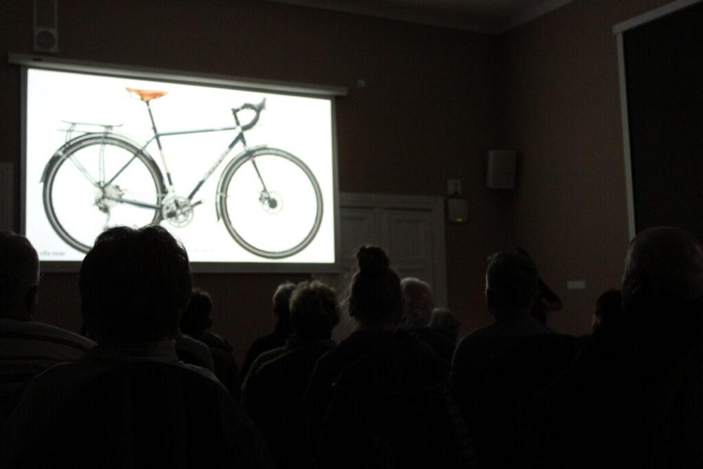 grupa widzów ogląda w ciemności prezentacje na zdjęciu rower