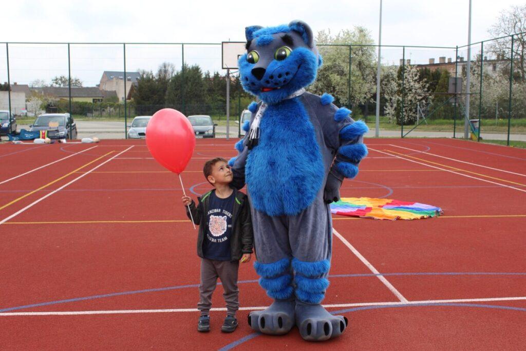 Boisko szkolne na świeżym powietrzu dziecko z balonem chłopiec pozuje do zdjęcia z dużą maskotką niebieskim kotem