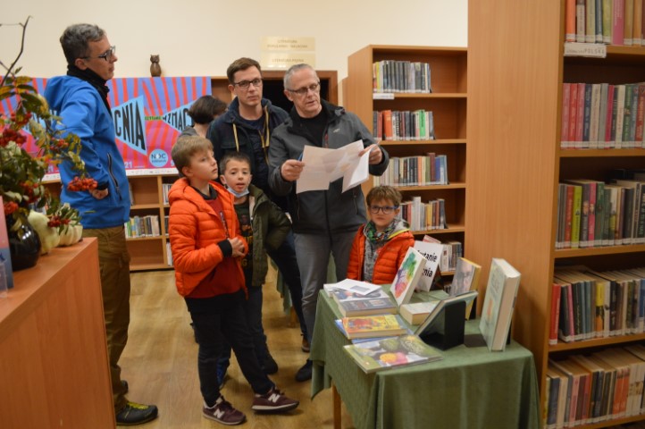 W wypożyczalni, Mężczyzna trzyma kartkę w dłoni. Dwaj mężczyźni oraz dwaj chłopcy stoją w pobliżu.