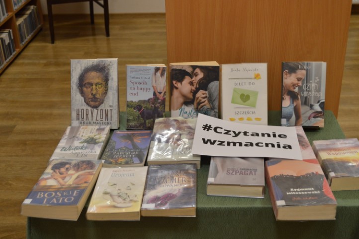 Na stole leżą książki oraz kartka z napisem #czytanie wzmacnia