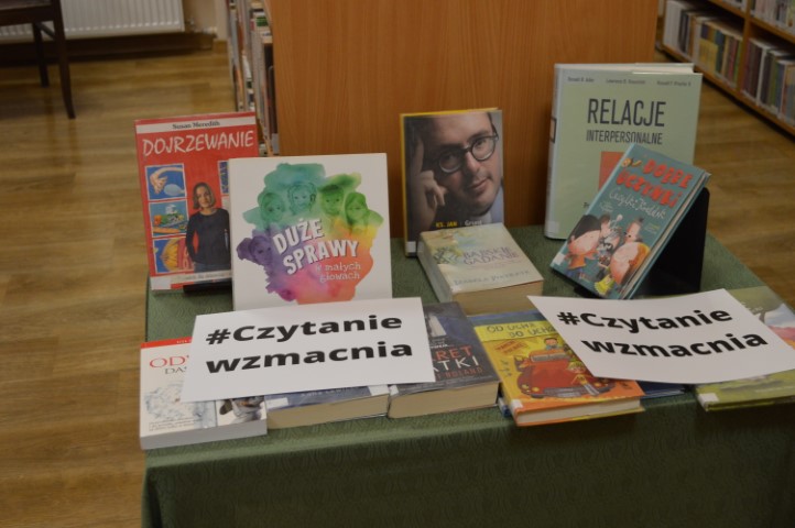 Na stole leżą książki oraz kartki z napisami #czytanie wzmacnia.