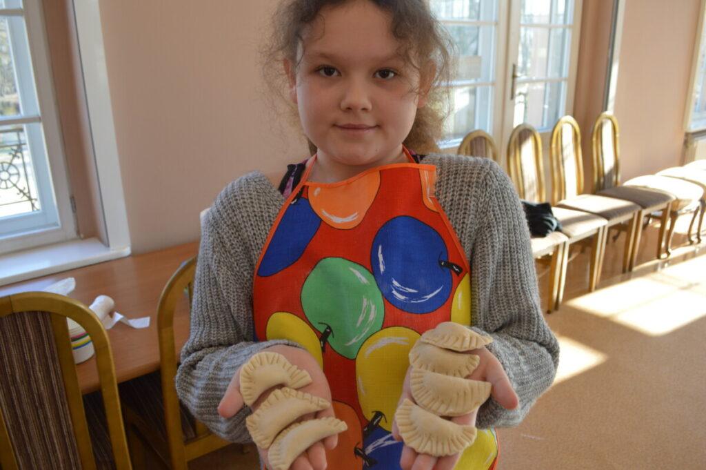 Ferie zimowe 2023 - dziewczynka trzyma ulepione przez siebie pierogi na zajęciach kulinarnych 