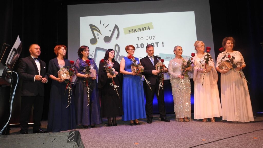 Chór Fermata - kobiety i mężczyźni dziesięć osób stoi na scenie z kwiatami