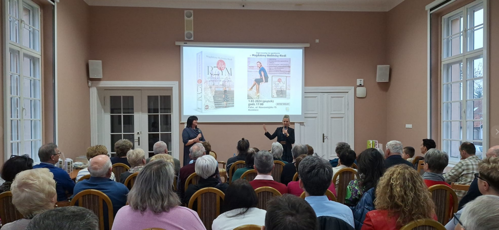 Grupa osób siedzi w budynku, przed nimi 2 kobiety stoją, przemawiają 
prezentacja w tle, tekst: Spotkanie z Magdaleną Wolińską-Riedi Książka "Mój Rzym".