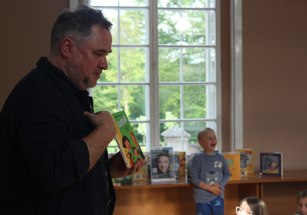 na pierwszym planie mężczyzna trzyma książkę  na drugim planie dziecko chłopiec śmieje się 
książki, okno w budynku