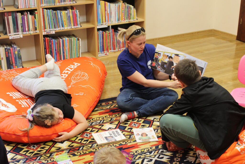 troje dzieci i kobieta siedzą na podłodze w budynku czytają książki 