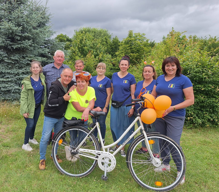 na powietrzu, grupa ludzi pozuje do zdjęcia 6 kobiet 3 mężczyzn przed nimi rower i pomarańczowe balony 