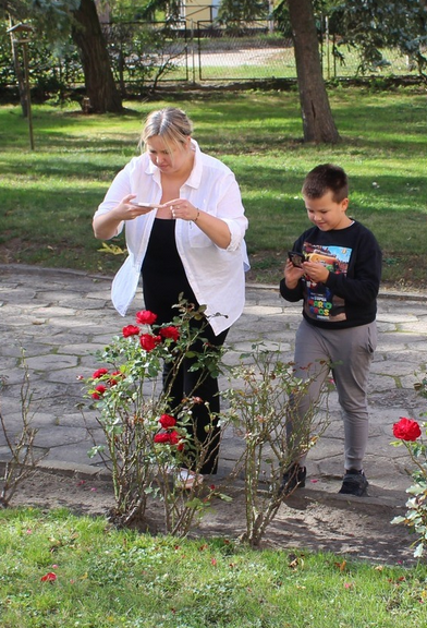 na zewnątrz kobieta i chłopiec nagrywają kwiaty telefonami