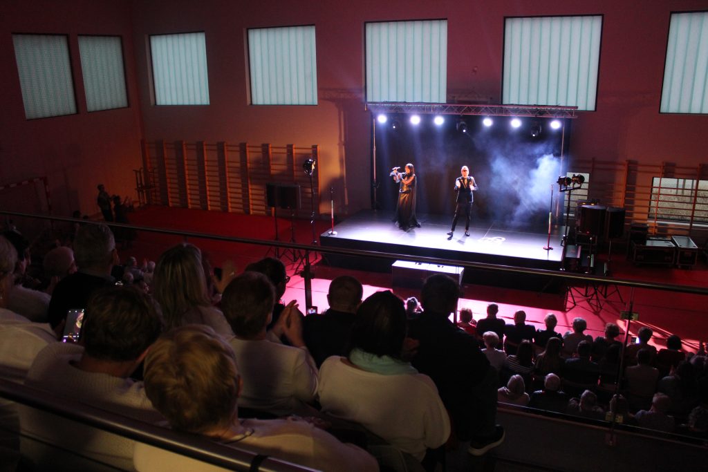 sala gimnastyczna, ludzie na krzesłach, scena, dwoje artystów