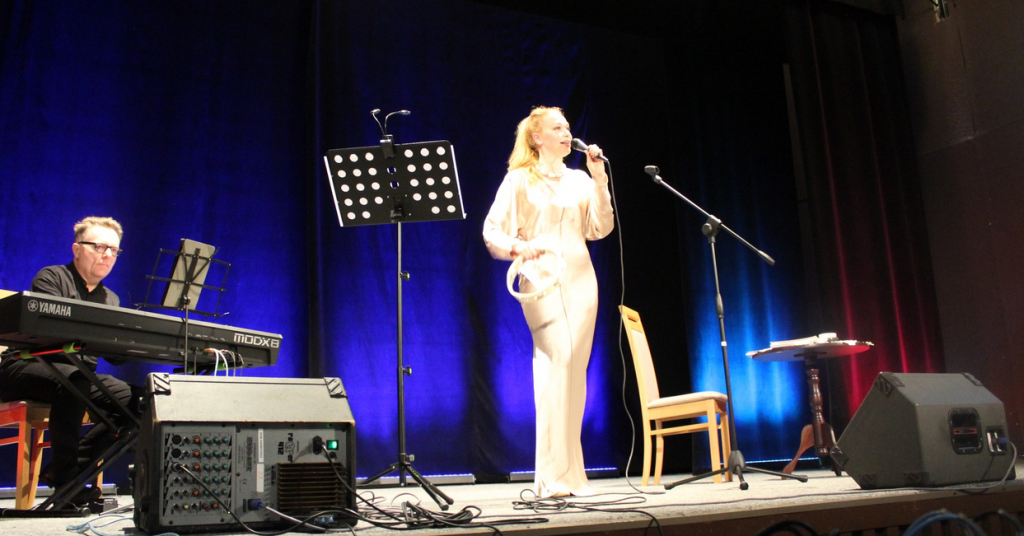śpiewaczka z tamburynem stoi i śpiewa - Marta Grabowska , na pianinie gra Jacek Skowroński , na scenie , w budynku