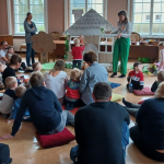 W budynku grupa dzieci i dorosłych kobieta pokazuje książkę