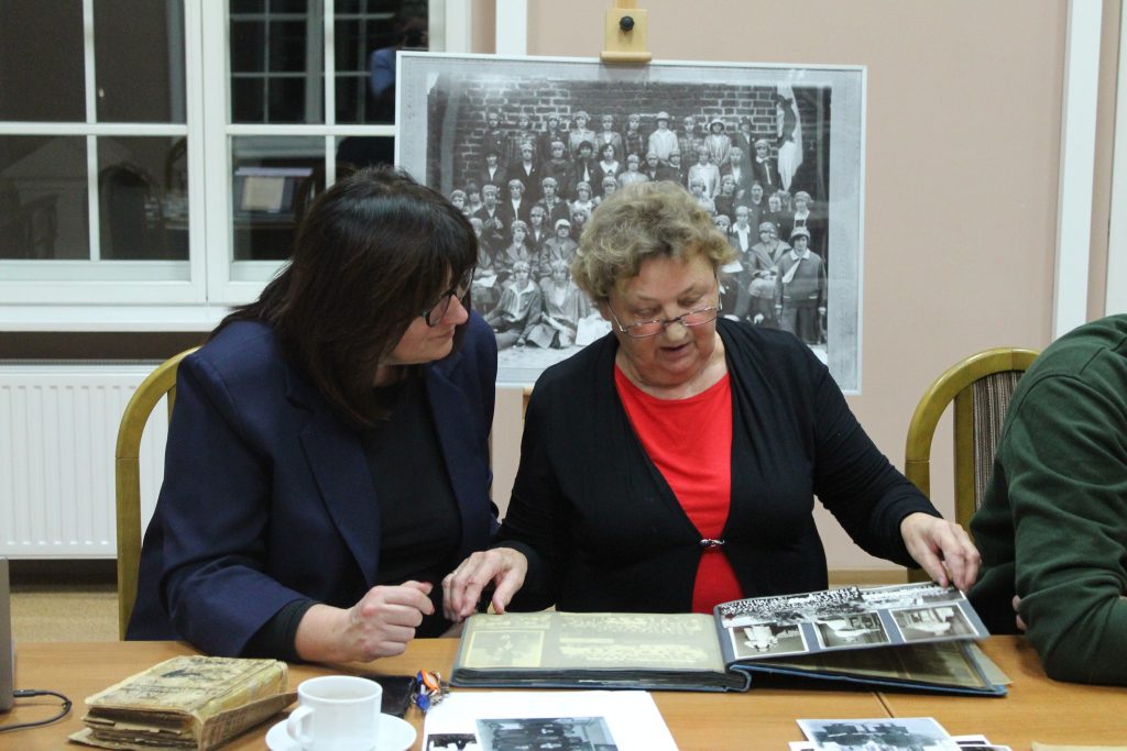 dwie kobiety siedzą przy stole oglądają album ze zdjęciami