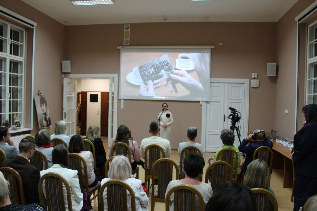 kobieta przemawia do siedzącej grupy ludzi w tle prezentacja starych zdjęć