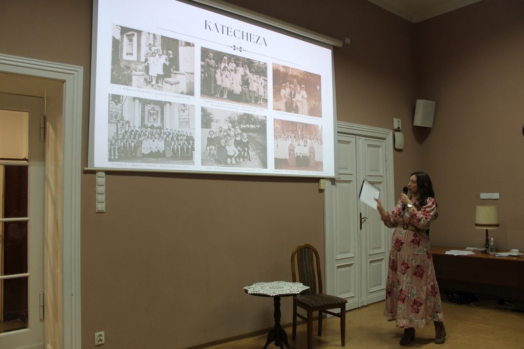 W sali prezentacja ze zdjęciami i prelegentka wskazuje na ekran