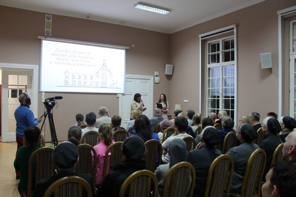 W sali grupa słuchaczy siedzi na krzesłach prezentacja ze zdjęciami i prelegentka wskazuje na ekran