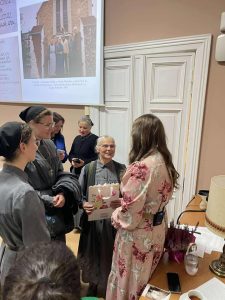 W tle prezentacja ze zdjęciami W sali 6 kobiet stoi w grupie