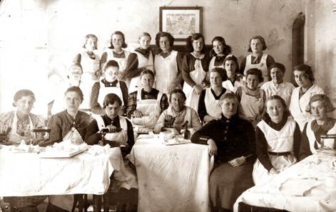 Kurs prania i prasowania sztywnej bielizny
grupa kobiet pozuje do zdjęcia
część siedzi za stołami na stołach żelazko i materiały