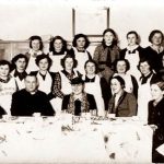 Dom Katolicki 1937. Kurs gotowania grupa kobiet i ksiądz pozują do zdjęcia część siedzi przy długim stole nakrytym białym obrusem na stole stoją karafki część kobiet stoi w drugim i trzecim rzędzie