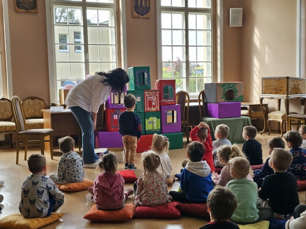 Grupa dzieci w sali Dziecko wskazuje na kolorowe pudła