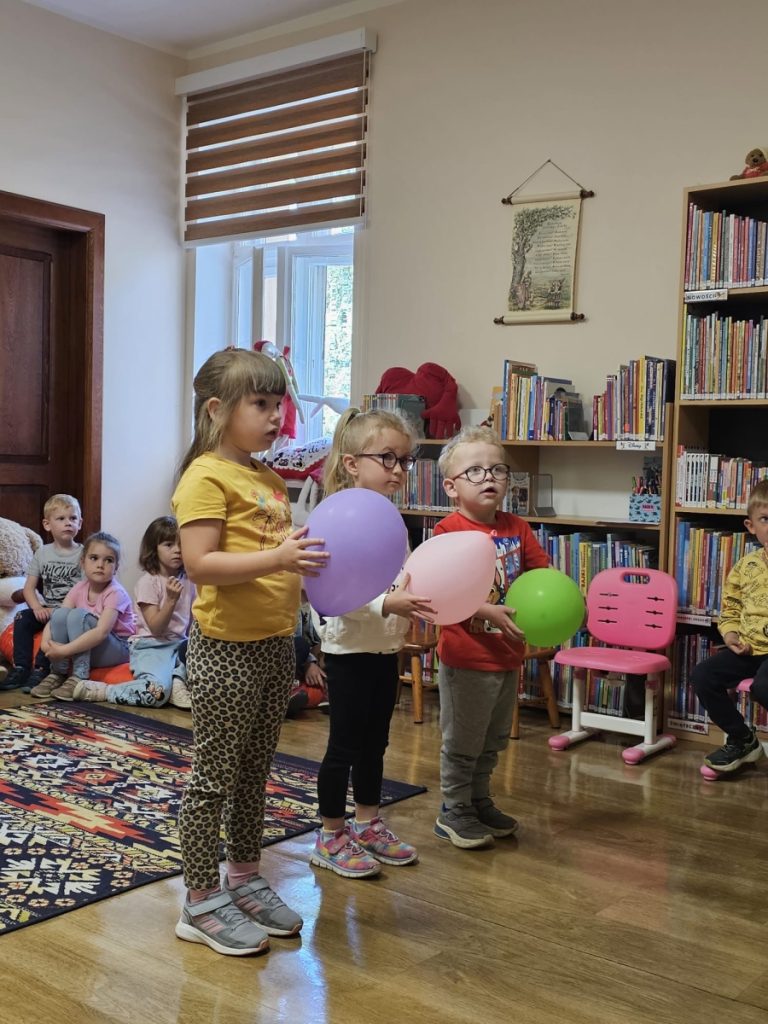 Grupa dzieci w sali trójka dzieci trzyma kolorowe balony