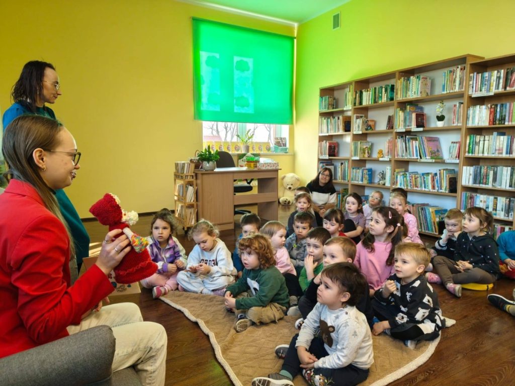 Kobieta pokazuje dzieciom książkę grupa dzieci siedzi na podłodze i sucha bajki