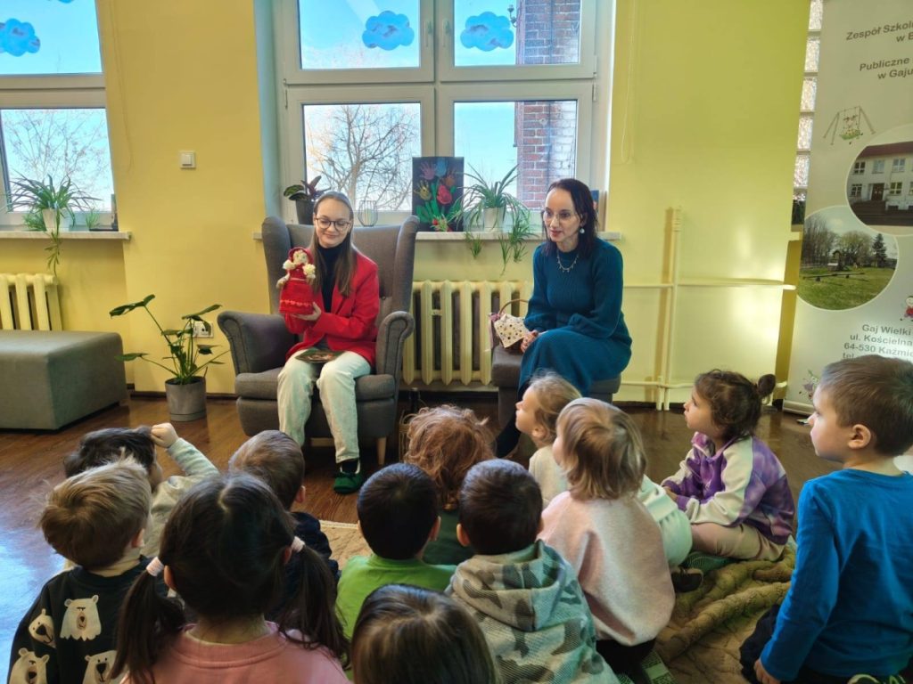 Kobieta pokazuje dzieciom książkę grupa dzieci siedzi na podłodze i sucha bajki