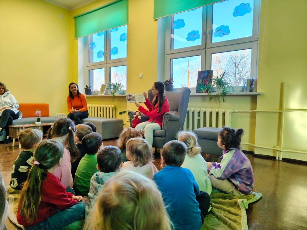 Kobieta pokazuje dzieciom książkę grupa dzieci siedzi na podłodze i sucha bajki