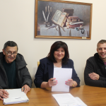 trzy osoby w budynku dwóch mężczyzn i kobieta siedzą przy stole podpisują dokumenty na ścianie obraz z książką