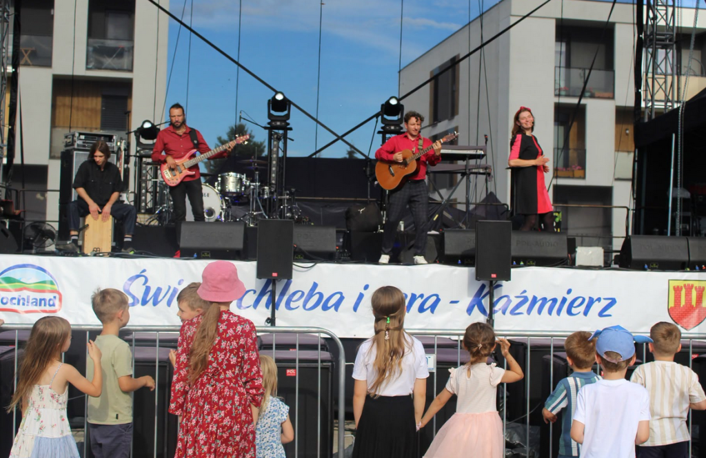SCENA W PLENERZE 5 OSÓB NA SCENIE, INSTRUMENTY
publiczność przed sceną